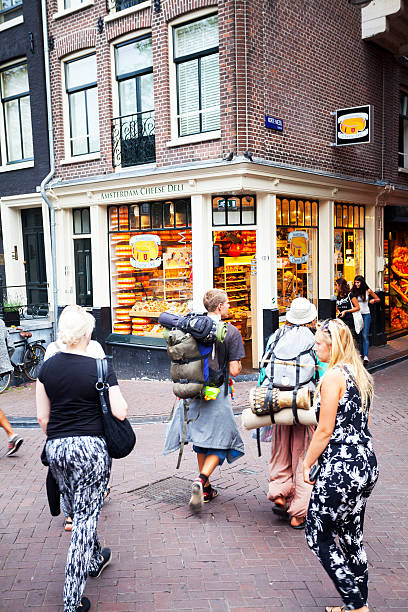 Backpacker couple in Amsterdam Amsterdam, The Netherlands - August 9, 2015: Rearshot of a walking young backpacker couple with backpacks walking in Wallen of Amsterdam in summer. In scene are some more people and tourists. In background is a chees store. wellen stock pictures, royalty-free photos & images