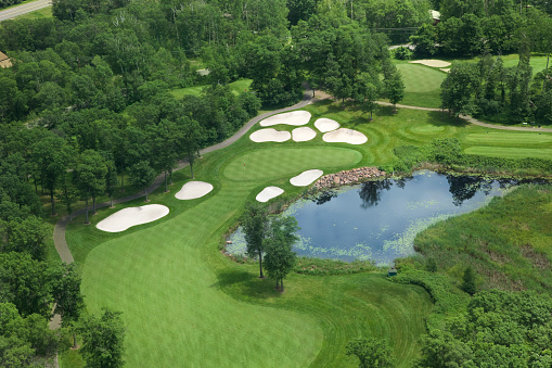 Aerial view of golf course fairway and green with sand traps, pond and trees