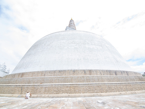Anuradhapura, Sri Lanka - February 24, 2015: Back view of woman praying at the Ruwanwelisaya Stupa in Anuradhapura, which is one of the world's tallest monuments in the world with 103 m or 338 feet. In background is light dramatic sky  while on left is part of another building.