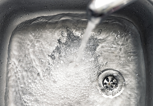Tapwater flowing into a kitchen sink and down the plughole.
