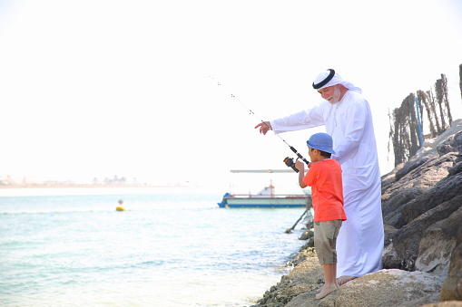 Arabian Grandfather and grandson fishing together on sea. 