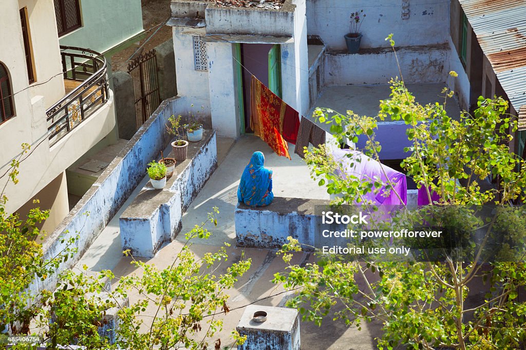 Indian woman sitting on roof top in Nimaj, India Nimaj, Rajasthan, India - March 7, 2015. High angle shot of an Indian woman in a sari sitting on a roof top in Nimaj, Rajasthan, India. 2015 Stock Photo