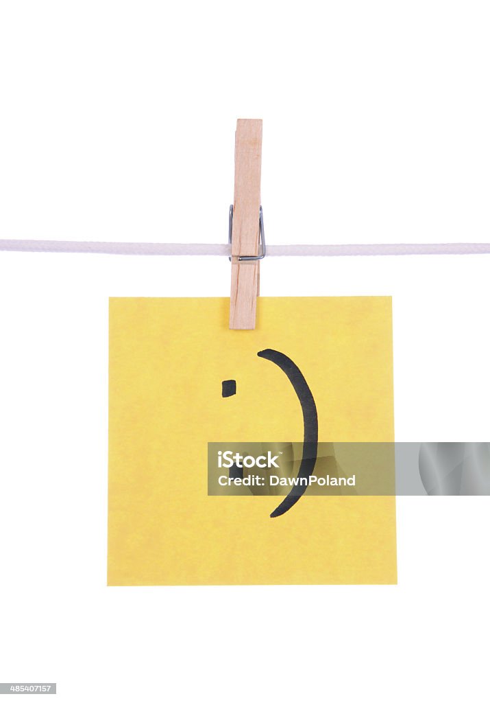 Texting Symbol Yellow paper with a smile texting symbol hand drawn on it hanging on a clothesline on a white background. Adhesive Note Stock Photo
