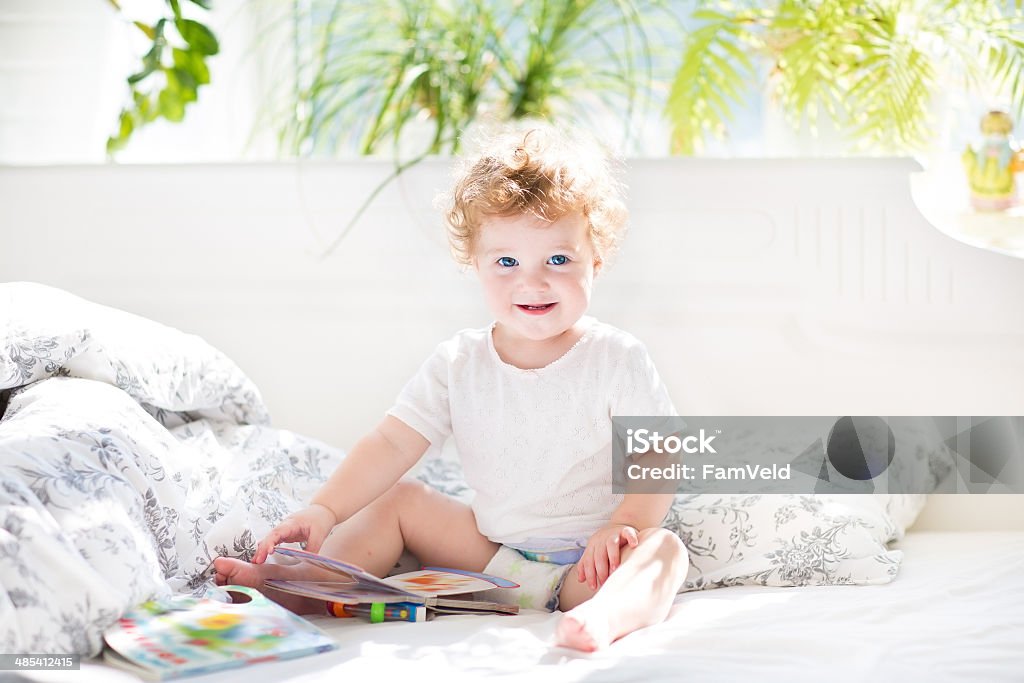 Happy funny baby reading book in her parents bed Happy funny baby reading a book in her parents bed on a sunny morning Baby - Human Age Stock Photo