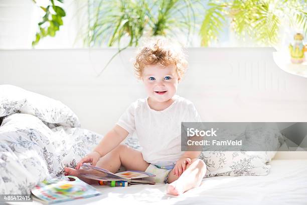 Happy Funny Baby Reading Book In Her Parents Bed Stock Photo - Download Image Now - Baby - Human Age, Bed - Furniture, Bedroom