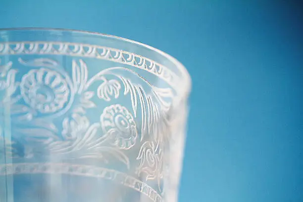 Macro closeup of decorative etching on wine goblet crystal glass against a blue background. Grain apparent at high resolution.