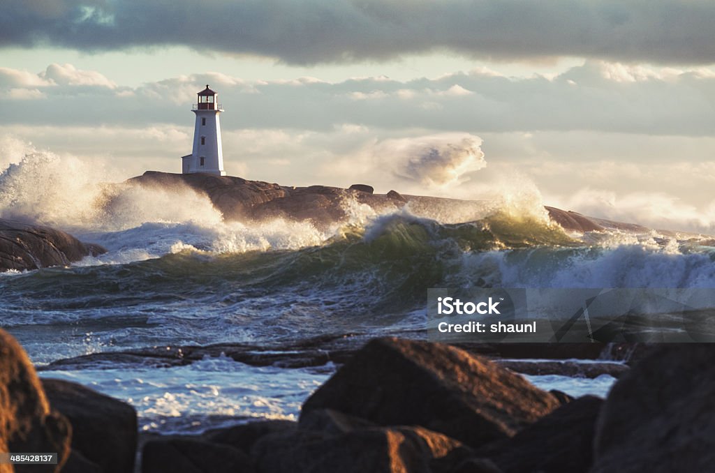 Sunlit Surf Heavy surf crashes ashore at Peggy's Cove Lighthouse during a strong Autumn storm. Lighthouse Stock Photo