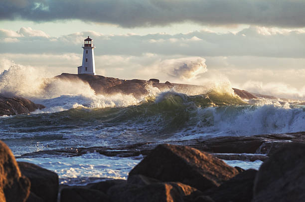 Sunlit Surf Heavy surf crashes ashore at Peggy's Cove Lighthouse during a strong Autumn storm. lighthouse stock pictures, royalty-free photos & images