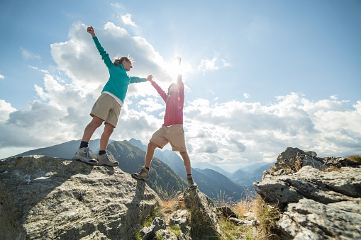 Couple of hikers reaching the mountain top celebrating. Arms outstretched for freedom and positive emotion.