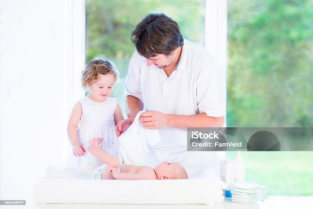 Linda menina, ajudando seu pai bebê de fralda irmão mudança - Foto de stock de Adulto royalty-free