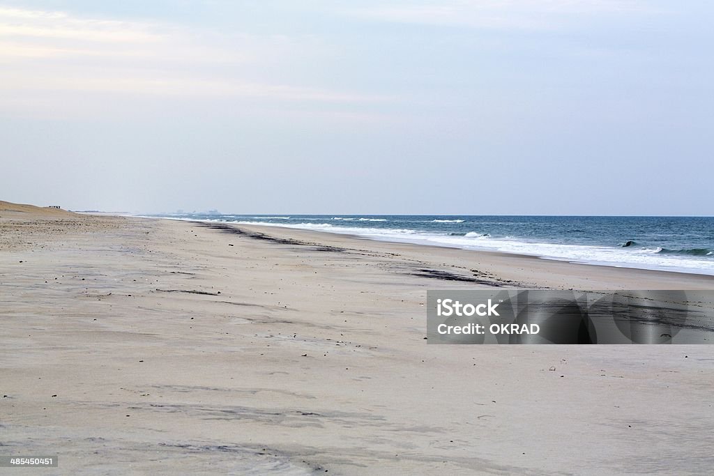 Atlantic Beach with no people Beach Scene taken on the Assateague National Seashore and park. This protected beach is on the Atlantic ocean and had no buildings on it. The low clouds have nice light pink and blue hues.  The beach is completely empty and there is a rich blue color of the water, and crisp white caps of the crashing waves. There are no people on the beach and you can barely make out Ocean City, Maryland in the background.  - A great coastal landscape taken in the outdoors. Ocean City - Maryland Stock Photo