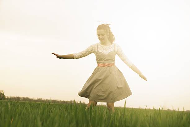 A serene woman in a white dress with a floral adornment stands in a verdant field, radiating tranquility. Capturing a blend of nature's simplicity and human connection to the outdoors.
