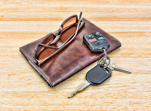 Sunglasses and car keys with leather wallet A set of car keys and tinted sunglasses atop a brown leather wallet on wood tabletop. car keys table stock pictures, royalty-free photos & images