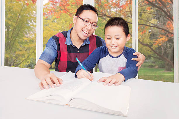 kleiner junge macht hausaufgaben mit eltern - reading and writing little boys reading asian ethnicity stock-fotos und bilder