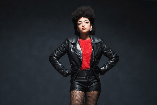 Half Body Shot of a Stylish Young African American Woman in Leather Jacket, Looking at the Camera Against Black Background.