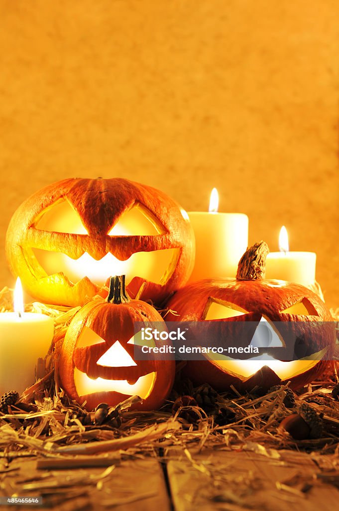 halloween pumpkins three illuminated halloween pumpkins and straw on old weathered wooden board in front of orange background in candlelight 2015 Stock Photo