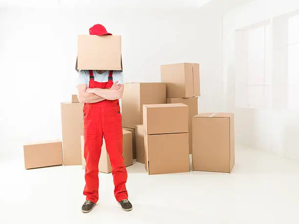 front view of deliveryman standing in new house with arms crossed against his chest, box covering his head