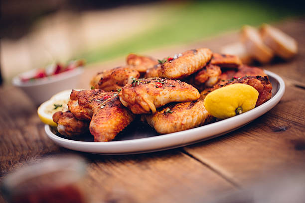 Barbecue grilled hot and spicy chicken wings seasoned with chillies and herbs with lemon on a plate on a wooden table