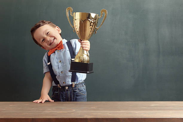 kleine junge raising einem goldenen trophäe - award trophy success achievement stock-fotos und bilder