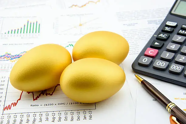Photo of Three golden eggs with a calculator on financial reports.