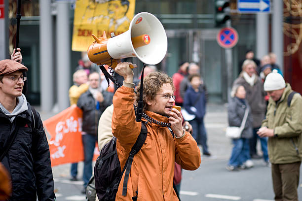 Frankfurt, Germany - November 12, 2011: Protestor speaking into a megaphone during 'Banken in die Schranken'-demonstration in the financial district of Frankfurt. The demonstration was - among others - organized by attac and Occupy Frankfurt, a german division of the international Occupy movement that began in New York as Occupy Wall Street. In the background groups of demonstrators
