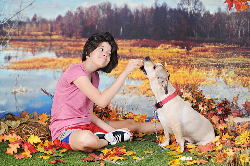 An attractive young teen rewarding her dog in the fall as they sit together by the edge of a pond.
