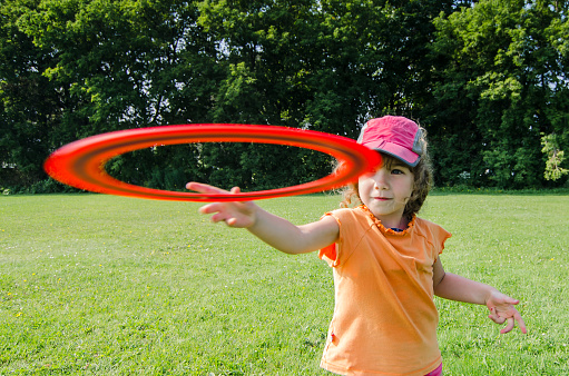Young girl, facing the camera, thorowing a flying disk (frisbee) in a field