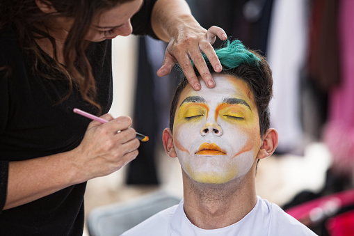 Young male clown getting makeup on face