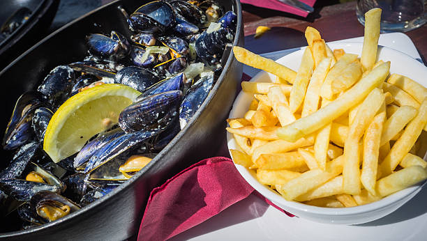 A large pan of Muscles   with a wedge of lemon and chips served out side