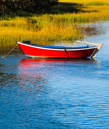 An old red dory is anchored on a tidal river on Cape Cod.