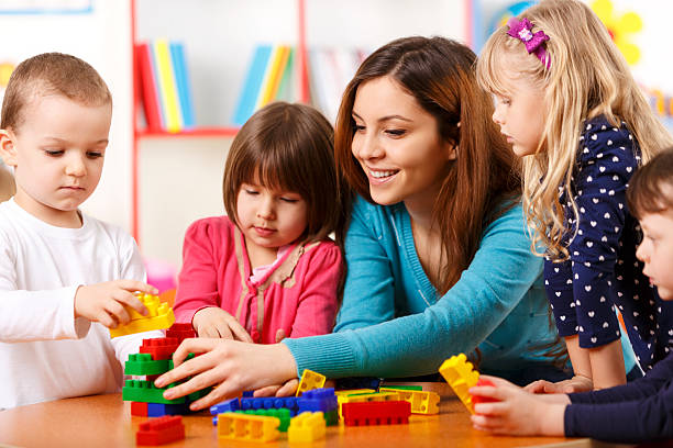 Nursery teacher and preschoolers playing with building blocks The image shows young and beautiful female  nanny stock pictures, royalty-free photos & images