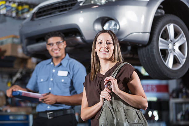 Customer at auto repair shop Hispanic woman (30s) at auto repair shop, with mechanic in background. Focus on woman. car mechanic top view stock pictures, royalty-free photos & images