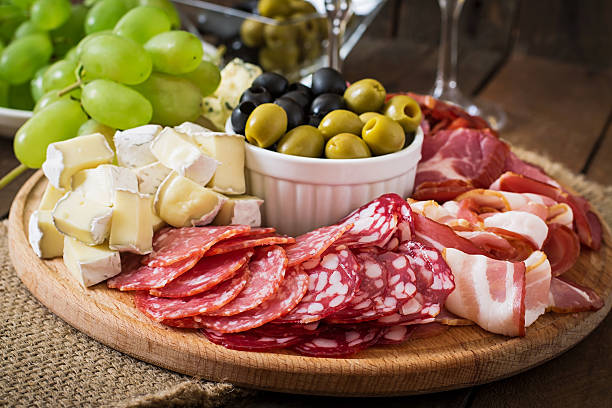 antipasti plateau de service traiteur avec du bacon, de viande séchée, du salami et fromage et raisins - entrée italienne photos et images de collection