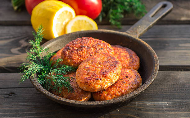 lachs-fischfrikadellen in gusseisen pfanne, tomaten und zitrone - fish cutlet stock-fotos und bilder