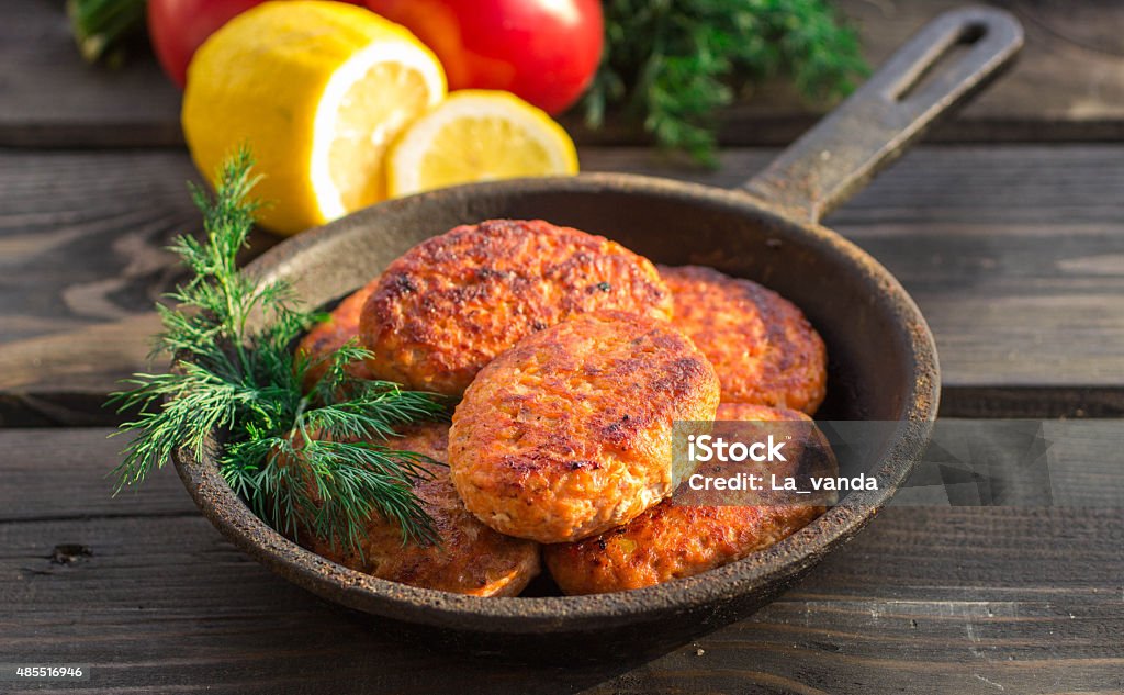 salmon fishcakes in a cast iron skillet, tomatoes and lemon salmon fishcakes in a cast iron skillet, tomatoes and lemon on a dark table. Selective focus Salmon - Seafood Stock Photo