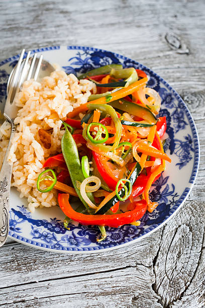 rice with roasted vegetables in Asian style on the enamel dish on dark wooden background