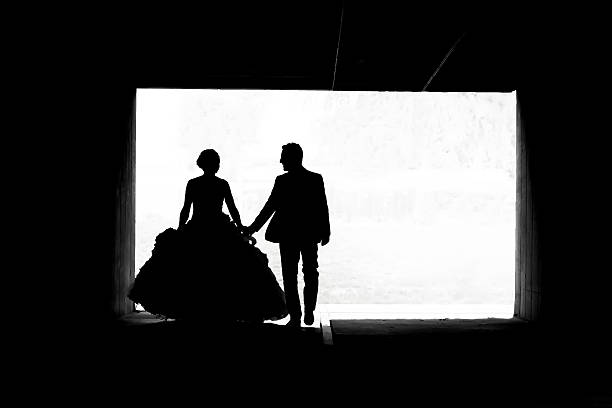 Silhouette of the bride and groom holding hands, looking at each other and walking in a passage under the overpass.