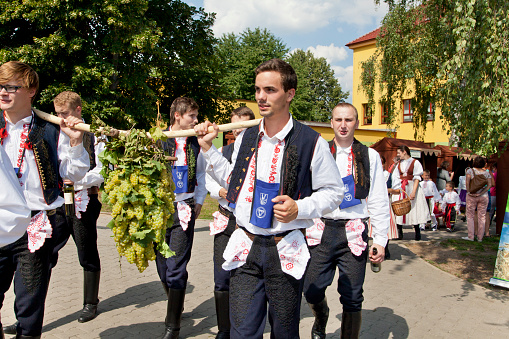Polešovice, Czech Republic - August 22, 2015: Members of folk dance group from Southern Moravia in the Czech Republic come in front of the procession on the feast of wine. They carry the flag of the city and a big bunch of grapes on a stick. They are dressed in beautiful multicolor folk costumes from southern Moravia. The traditional ceremony took place in Polešovice in southern Moravia in the Czech repiblice.