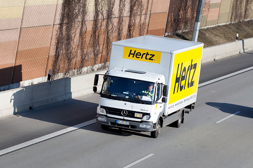 Wallau, Germany - February 3, 2012: A middle-aged men in a small truck of car rental company Hertz on german autobahn A66 near Wiesbadener Kreuz. The pictured tractor is a MAN truck. MAN is a german automobile manufacturer specialised in trucks and buses. It was founded in 1758 and is headquartered in Munich. Minor motion blur.
