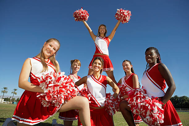 Happy Cheerleaders Holding Pompoms On Field Low angle view of happy young cheerleaders holding pompoms on field cheerleader photos stock pictures, royalty-free photos & images
