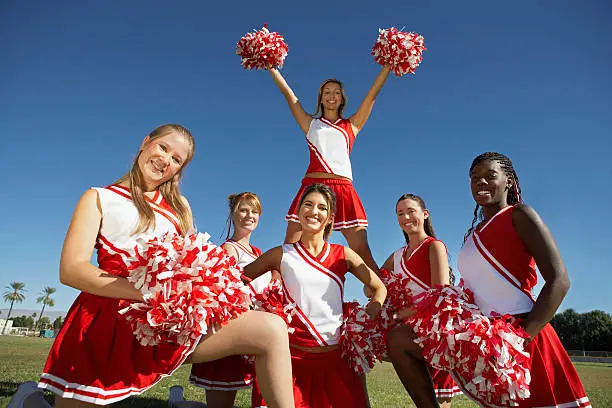 Low angle view of happy young cheerleaders holding pompoms on field