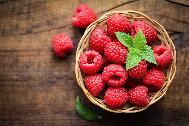 Fresh raspberries Fresh ripe red raspberries in a wicjer bowl on dark rustic wooden background raspberry stock pictures, royalty-free photos & images