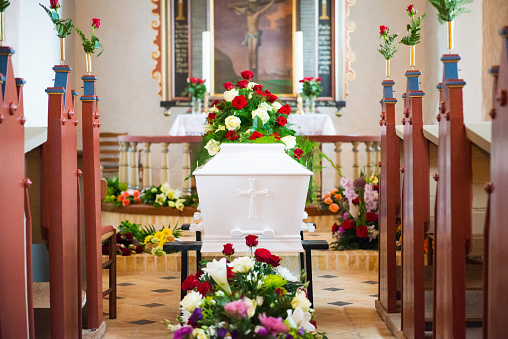 Looking down the church floor, full of flowers. Coffin by the end. 