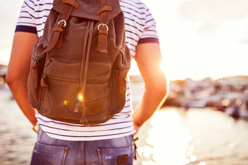 Hipster Traveler with backpack and outspread hands near sea at sunrise. Enjoying sun, deep breathing