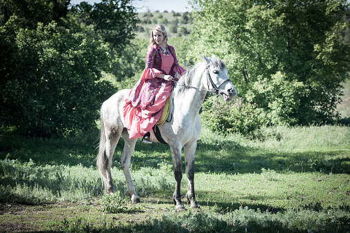 Horsewoman in pink dress on horseback in green forest