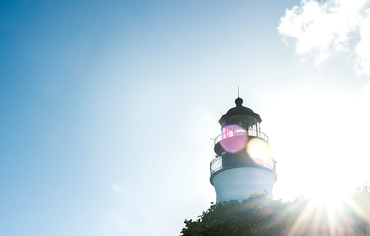 This is a horizontal, color, royalty free stock photograph of the bright afternoon sun shining behind the landmark Key West lighthouse on a hot summer day. A lens flare is cast across the architecture and clear blue sky in this tropical USA travel destination. Photographed with a Nikon D800 DSLR camera.