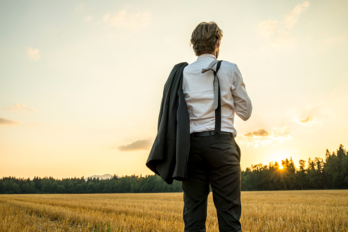 Young successful businessman standing in wheat field looking gazing into the future as he decides upon new steps and directions to take in his career.