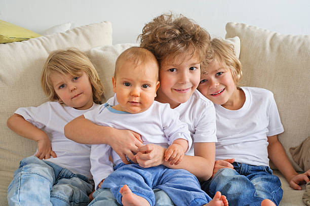 Four brothers on a couch Four brothers, young boys, sitting on a sofa. The eldest is holding a baby in his lap.  They're looking at the camera 6 9 months stock pictures, royalty-free photos & images