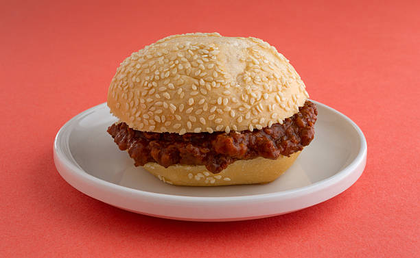 Sloppy joe sandwich on a small plate A freshly made sloppy joe sesame seed roll sandwich on a small plate atop an orange table top. sloppy joes stock pictures, royalty-free photos & images