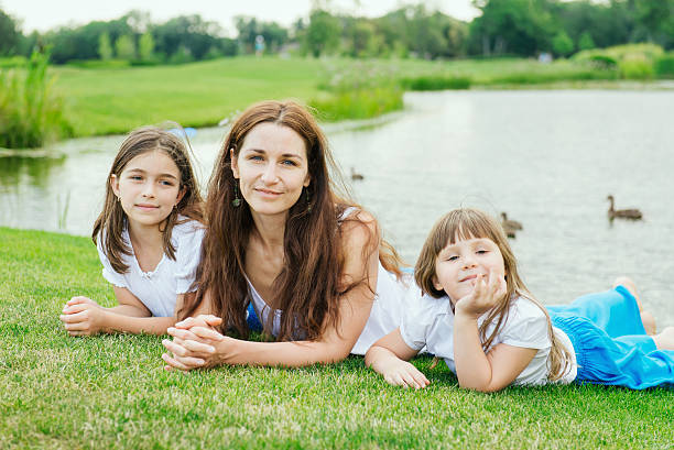 istock Mother with two daughters lie on the grass near lake 485571946